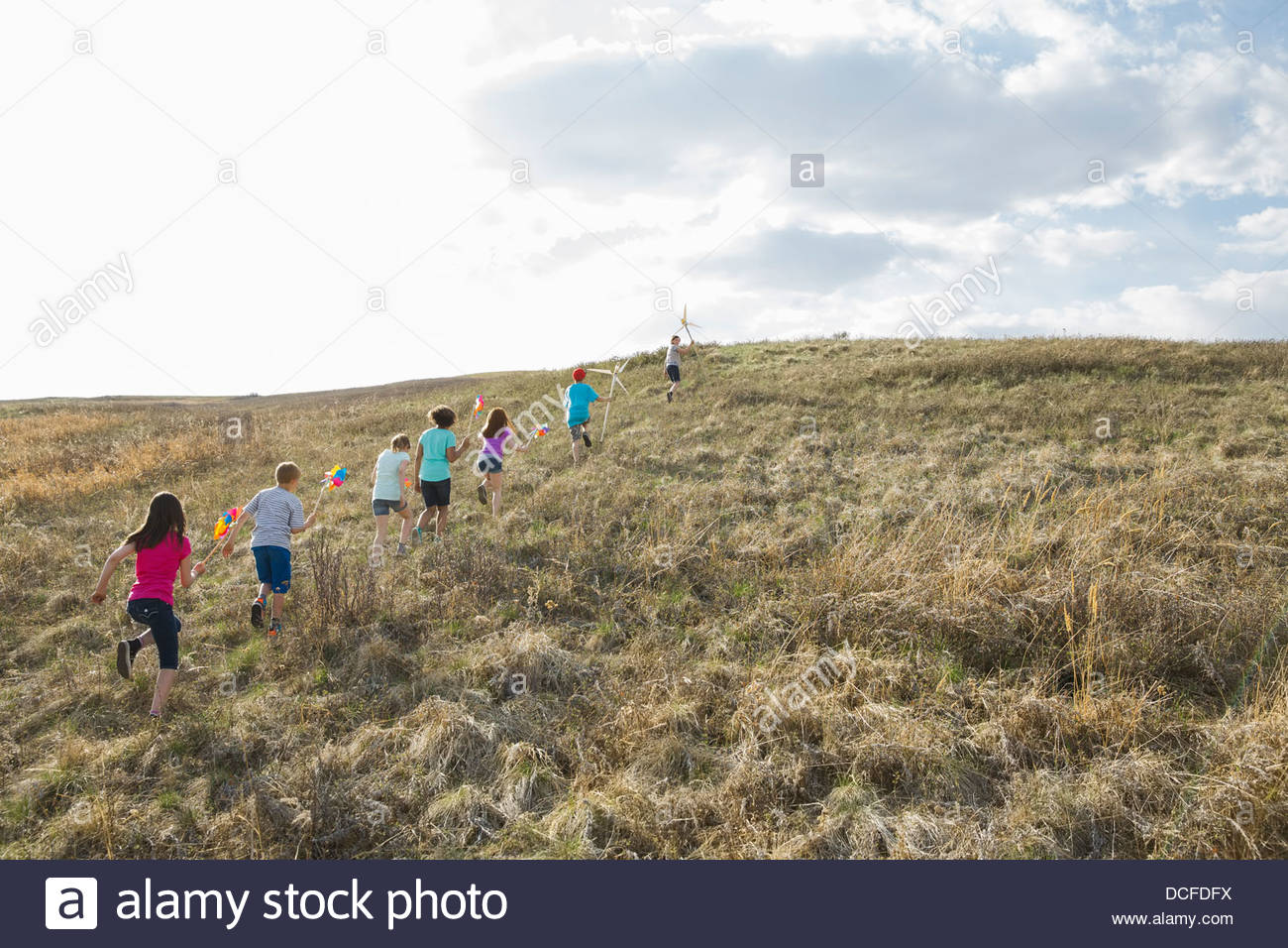 Los niños caminando cuesta arriba con molinetes y molinos de viento Foto de stock