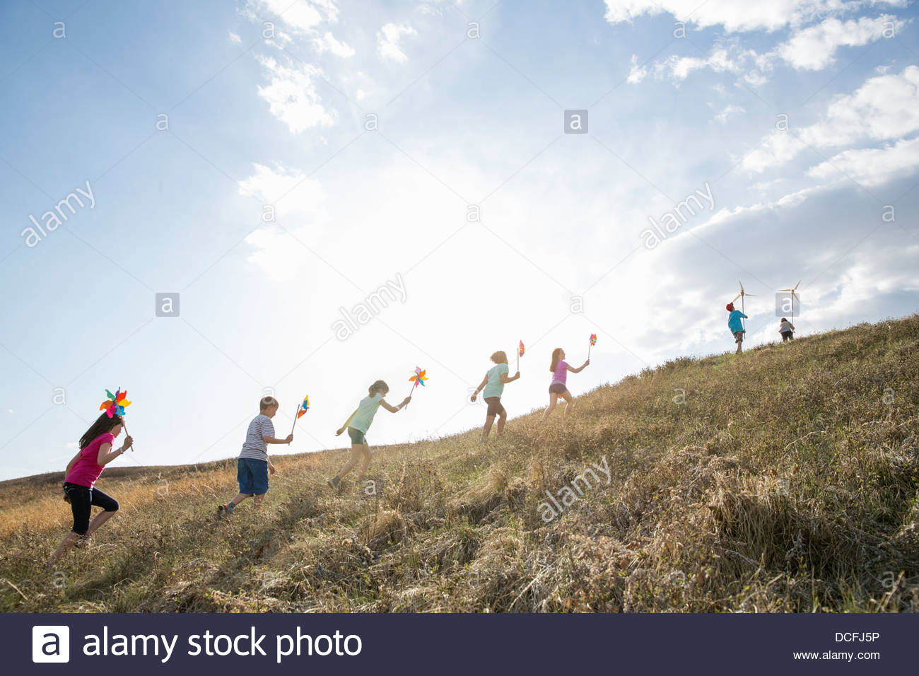 Los niños caminando cuesta arriba con molinetes y modelos de aerogeneradores Foto de stock