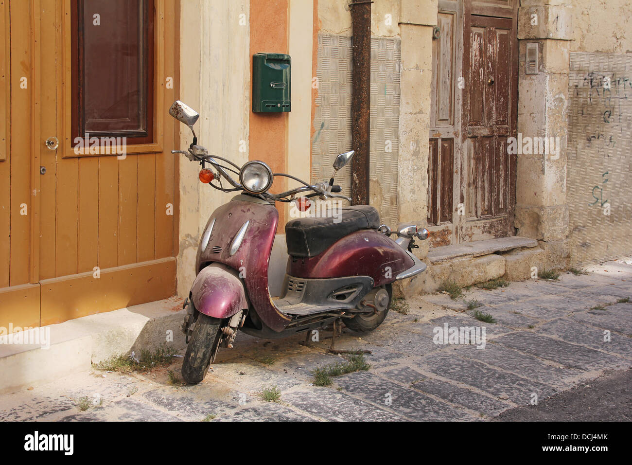 Old rusty púrpura oldtimer scooter moto dejó en una calle abandonada Foto de stock