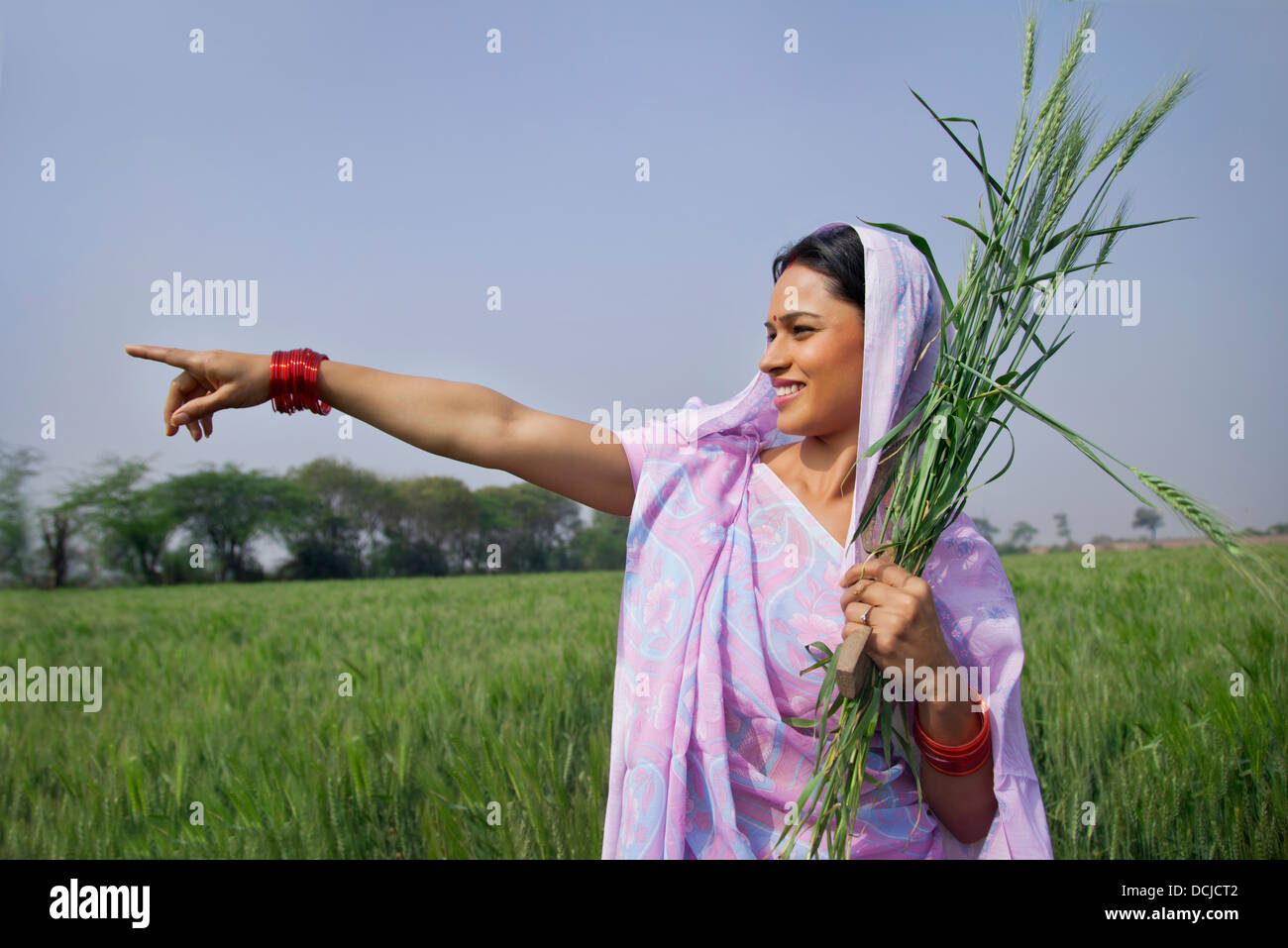 Feliz trabajadora agrícola indio apuntando a algo mientras está de pie en el campo Foto de stock