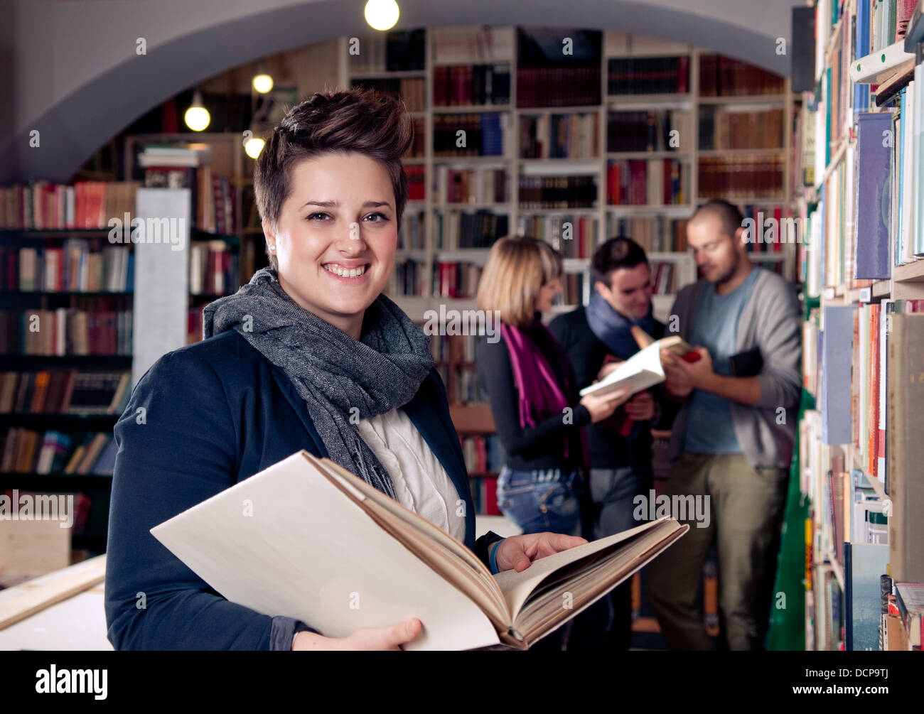 Sonriendo estudiante femenina la celebración de libro. Estudiantes en el fondo. Foto de stock