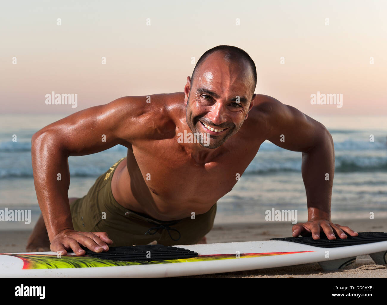 Un hombre inclinado sobre su tabla de surf en la playa, Tarifa, Cádiz, Andalucía, España Foto de stock