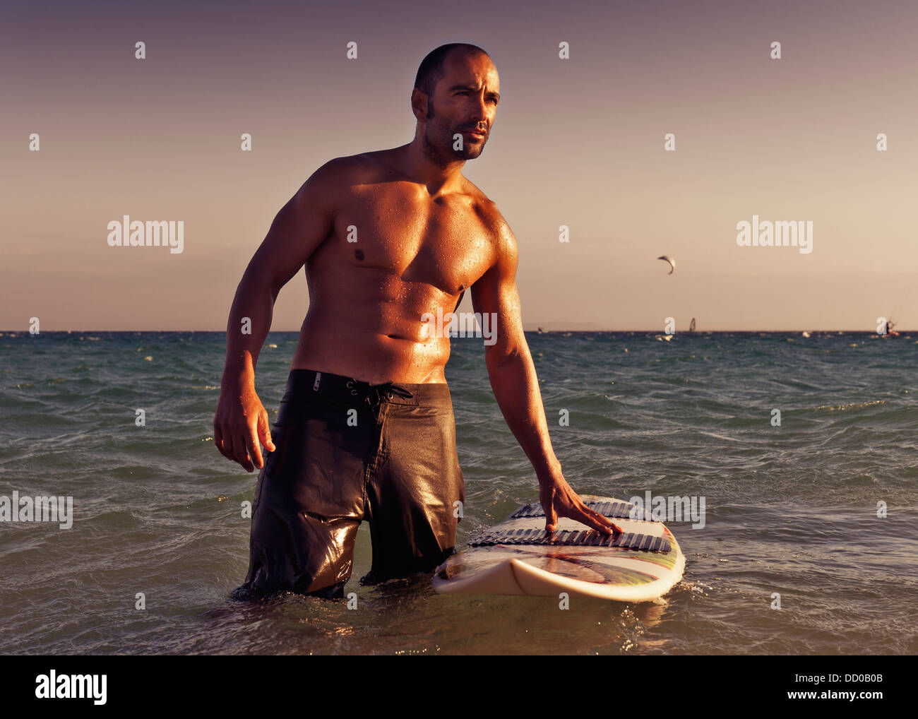 Un hombre con su tabla de surf en el agua al atardecer, Tarifa, Cádiz, Andalucía, España Foto de stock