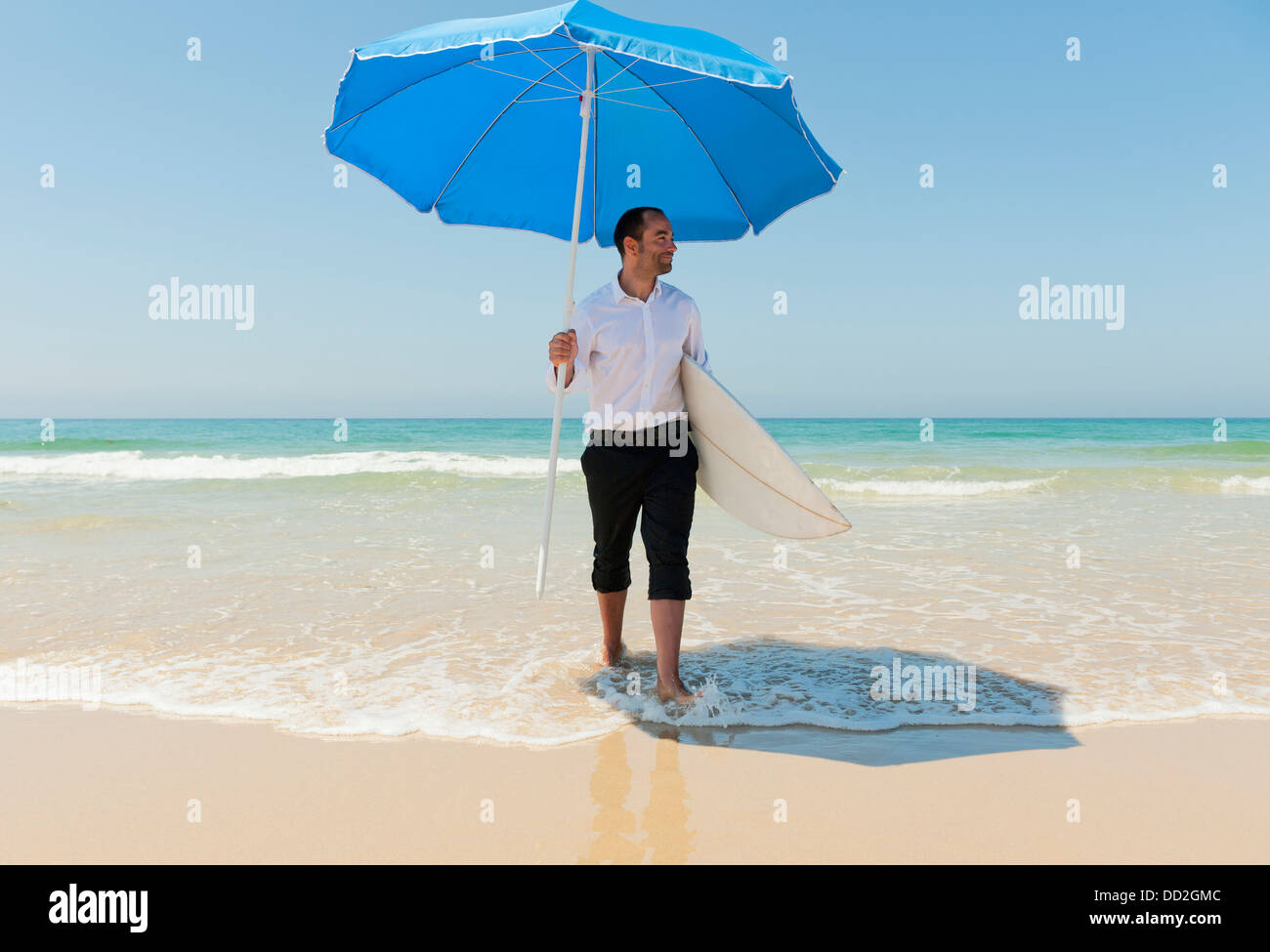 Un empresario en la playa sosteniendo una sombrilla en la playa y surf; Tarifa, Cádiz, Andalucía, España Foto de stock