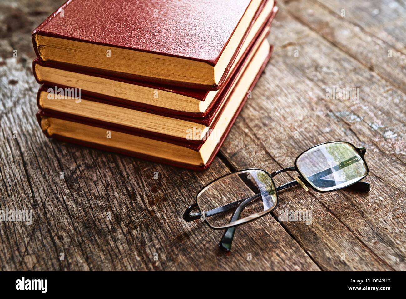 Libros y gafas de lectura sobre la mesa. Pila de libros de tapa dura sobre la mesa de madera antigua. Foto de stock