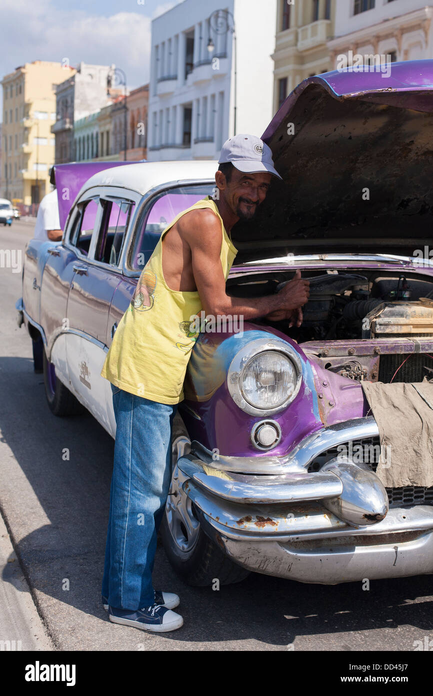 Un hombre trabaja en el motor de un coche clásico americano en la calle con el capó y criado en La Habana, Cuba Foto de stock