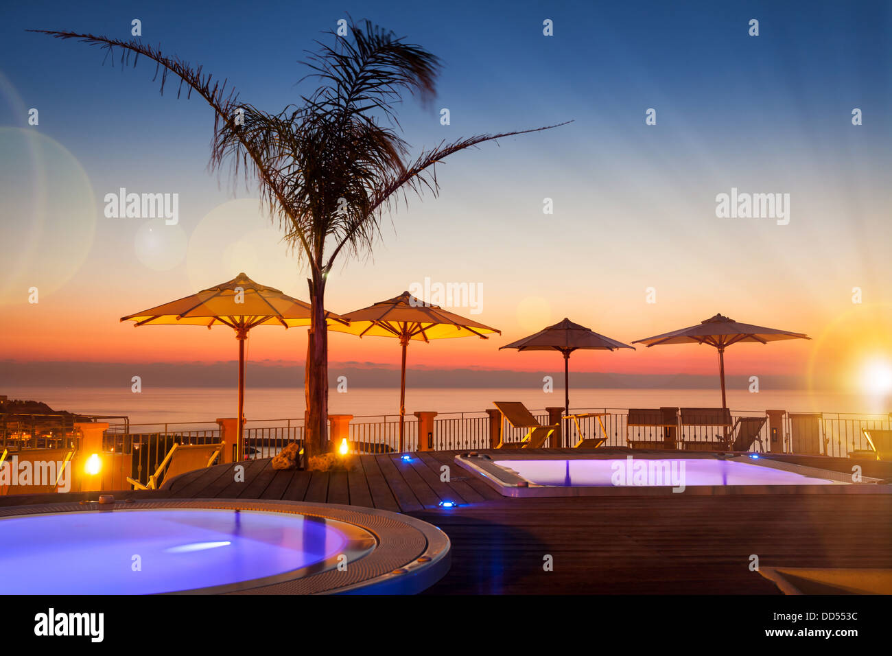 Hora de verano: hermosa vista del amanecer rojo en la zona de la piscina con palmeras y sombrillas en Foto de stock