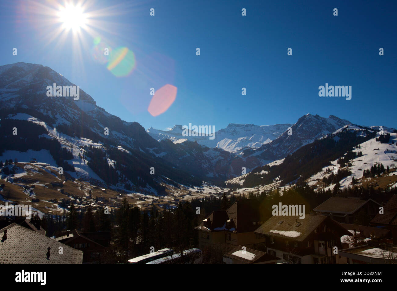 Sunburst y cámara luminosa sobre nevadas montañas suizas con el cielo azul Foto de stock