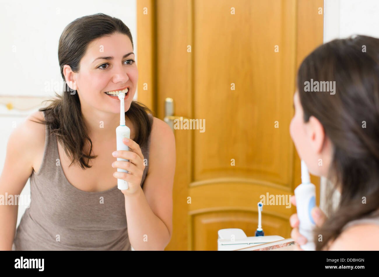 Bella mujer cepillarse los dientes mirándose en el espejo Foto de stock
