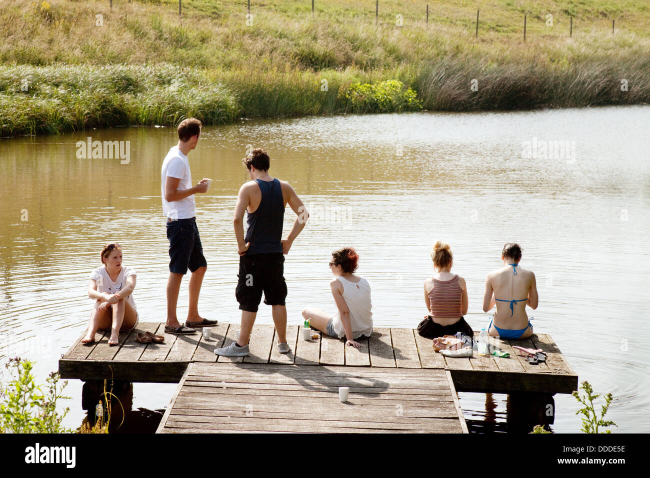 Verano del Reino Unido; un grupo de adolescentes pasando el rato y hablando en un embarcadero junto a un lago en verano, Lambourn, Berkshire Inglaterra Reino Unido Foto de stock