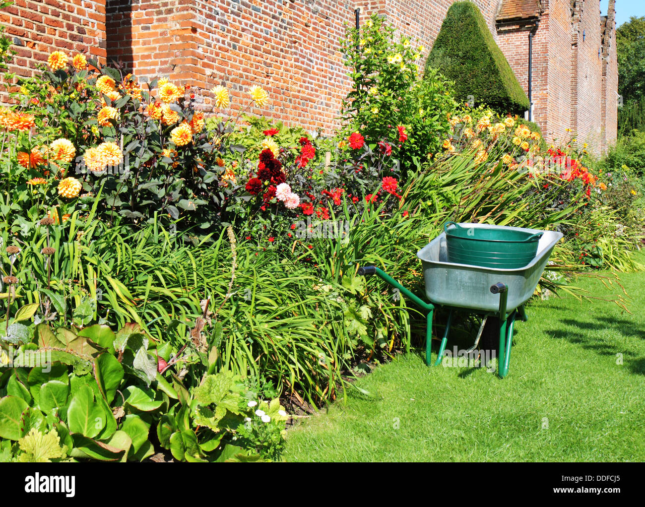 Carretilla de mano aparcado al lado de una frontera de coloridas flores de verano en un jardín inglés Foto de stock