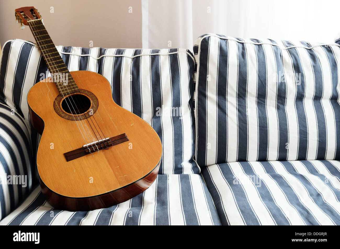 Guitarra acústica en un sofá, rayas horizontales Foto de stock