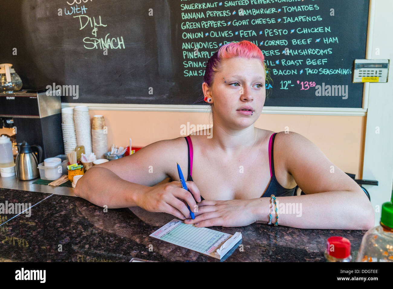 Hipster chica en sus veinte años, que trabaja en la tienda de helados y tiene piercings y multi-color del cabello. Foto de stock