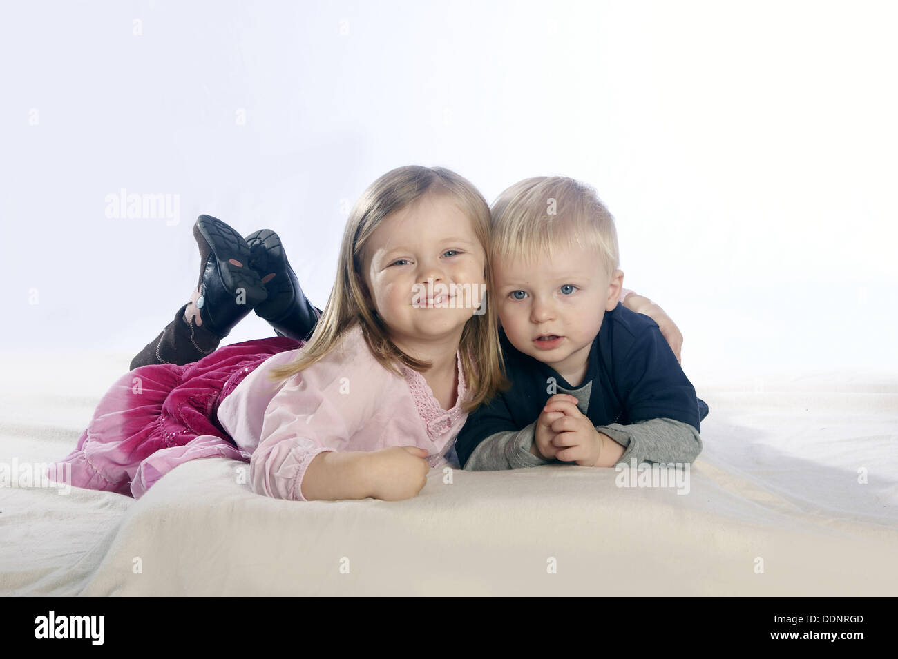Hermosa niña de 3 años de edad con el pelo rubio , sonriendo a la cámara,  en el estudio,tumbado en el suelo con su bebé de 2 años Fotografía de stock  - Alamy