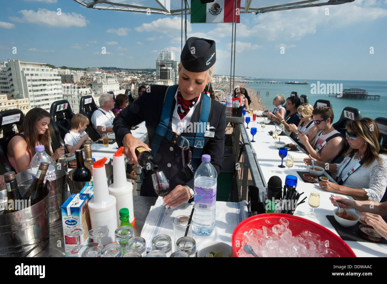 Una azafata de BA sirviendo bebidas a los comensales en una mesa de restaurante colgando de una grúa, 100 pies por encima de la playa de Brighton. Foto de stock