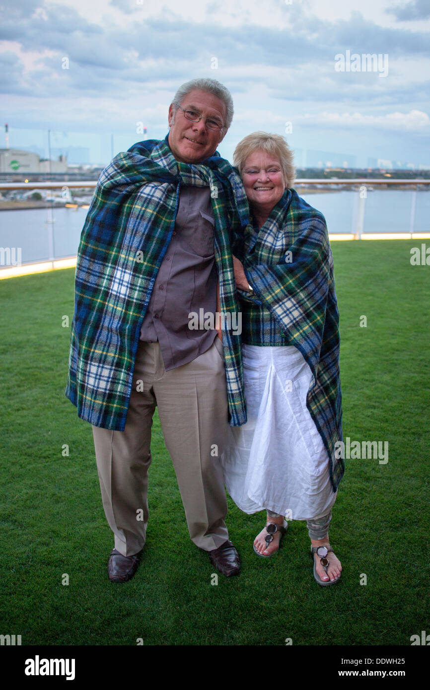 Feliz pareja de mediana edad de pie junto con toallas, alfombras de tartán envuelto alrededor de ellos mientras está de pie sobre el césped Foto de stock