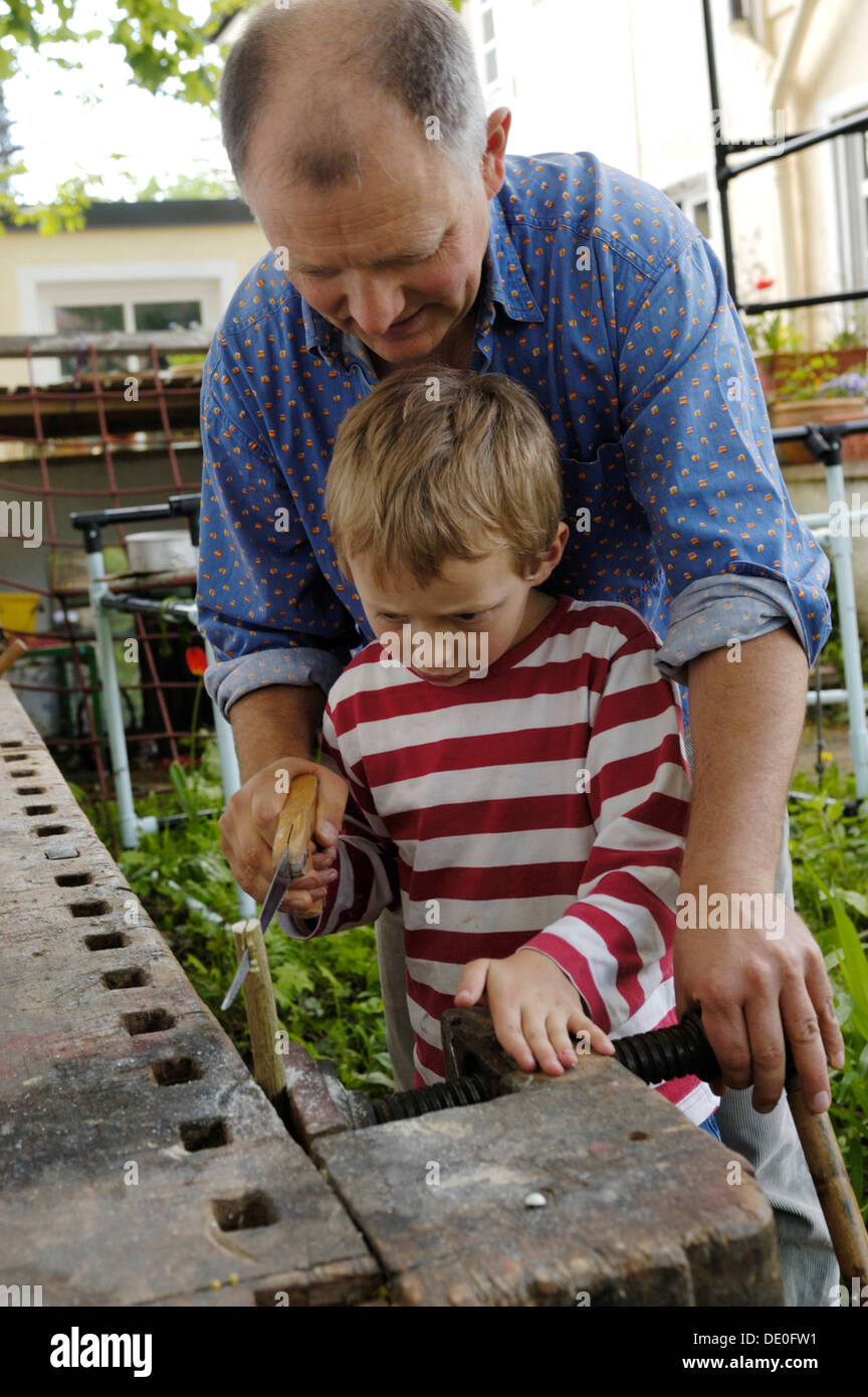 Padre serrar madera con su hijo pequeño, 7, sobre un banco de trabajo Foto de stock