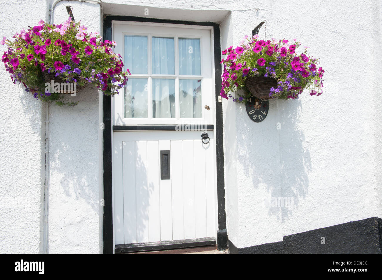 Puerta blanca con marco negro, paredes encaladas y flores colgantes en la  callejuela en Dunsford, REINO UNIDO Fotografía de stock - Alamy