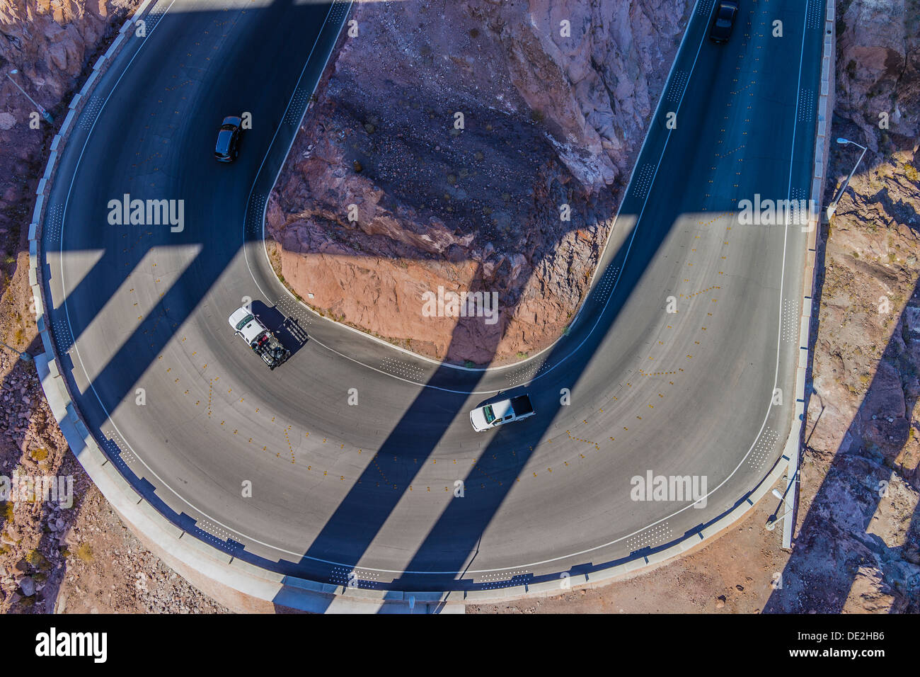 Vista aérea de una curva de herradura a Hoover Dam con vehículos blancos conducir alrededor de curva con largas sombras lineales. Foto de stock