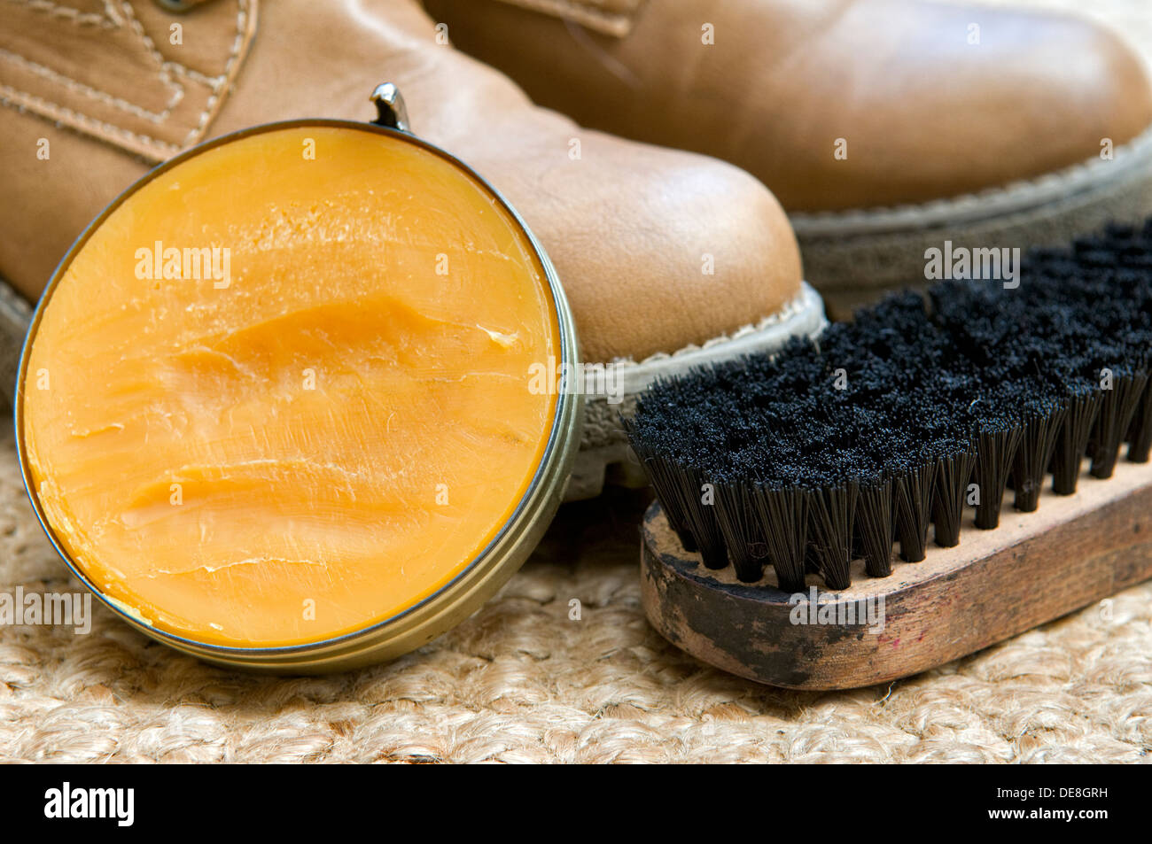 Betún marrón con un cepillo y un par de botas a la espera de ser pulido en estera tejida Foto de stock