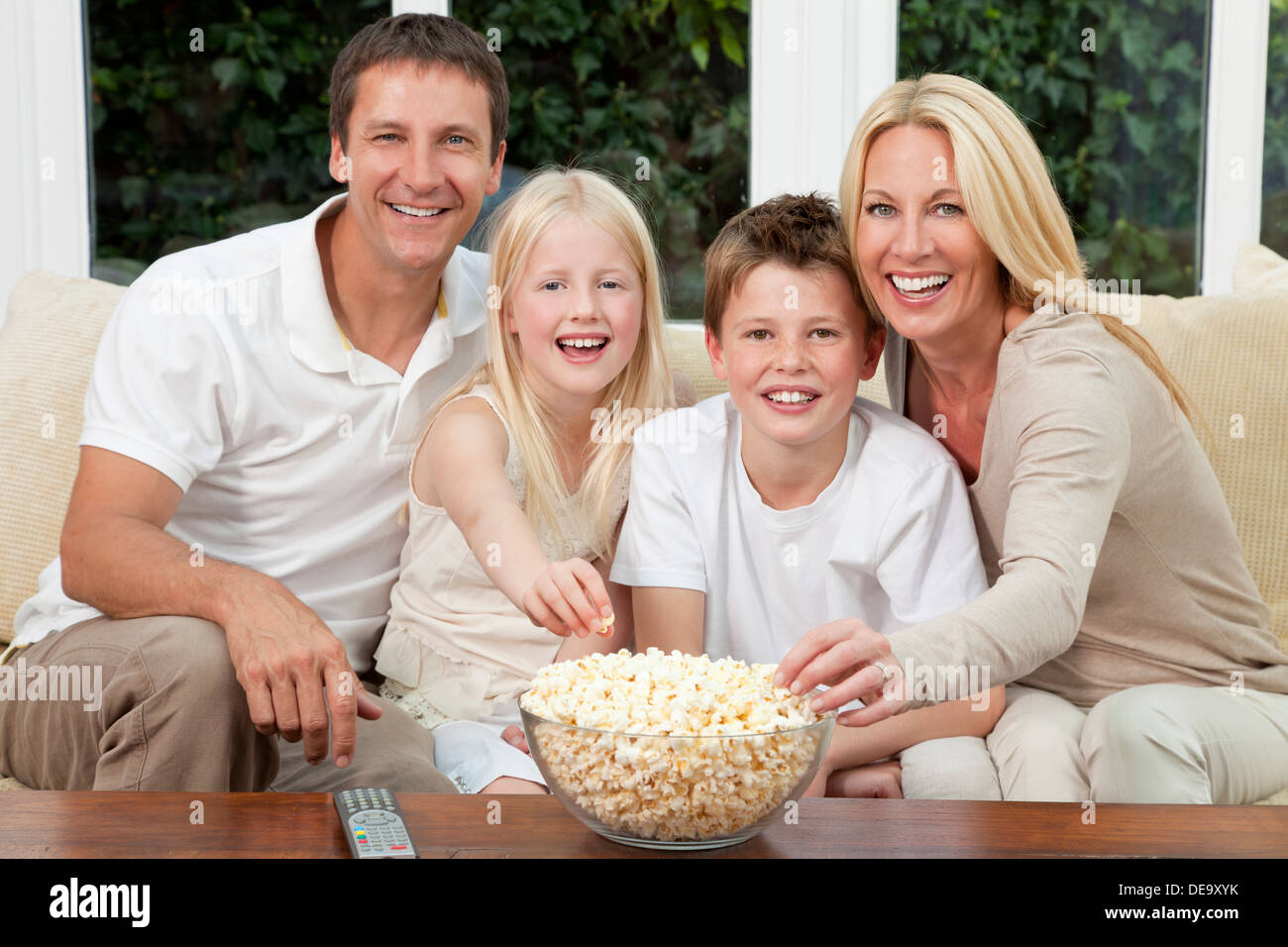 Feliz familia de padre, madre, hijo e hija sentado en un sofá en casa  viendo una película o la televisión y comiendo palomitas de maíz Fotografía  de stock - Alamy