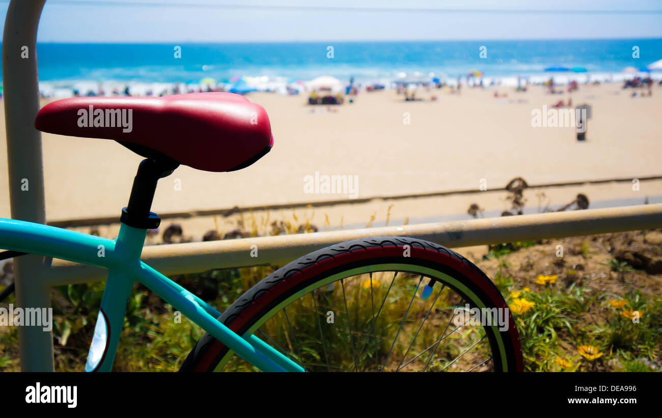 Teal y bicicleta roja inclinada contra una valla con vistas a la playa Foto de stock