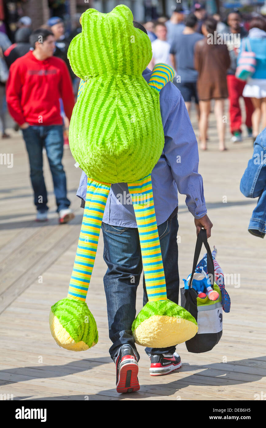 Hombre caminando por un paseo marítimo con un animal de peluche rana gigante  colgado en su espalda Fotografía de stock - Alamy