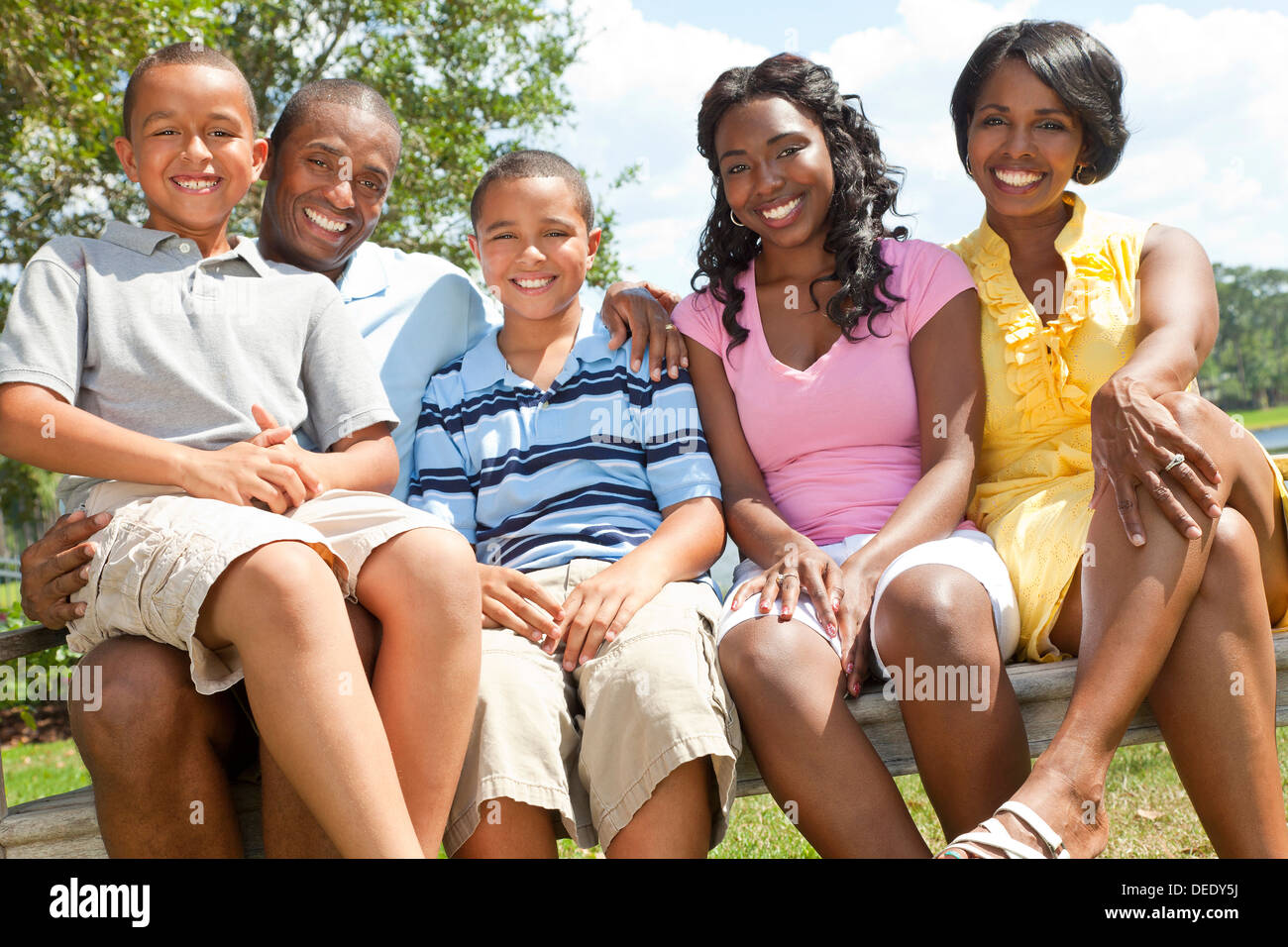 Una feliz familia americana africana negra de dos padres y tres hijos, dos chicos una chica, sentados juntos en el exterior. Foto de stock