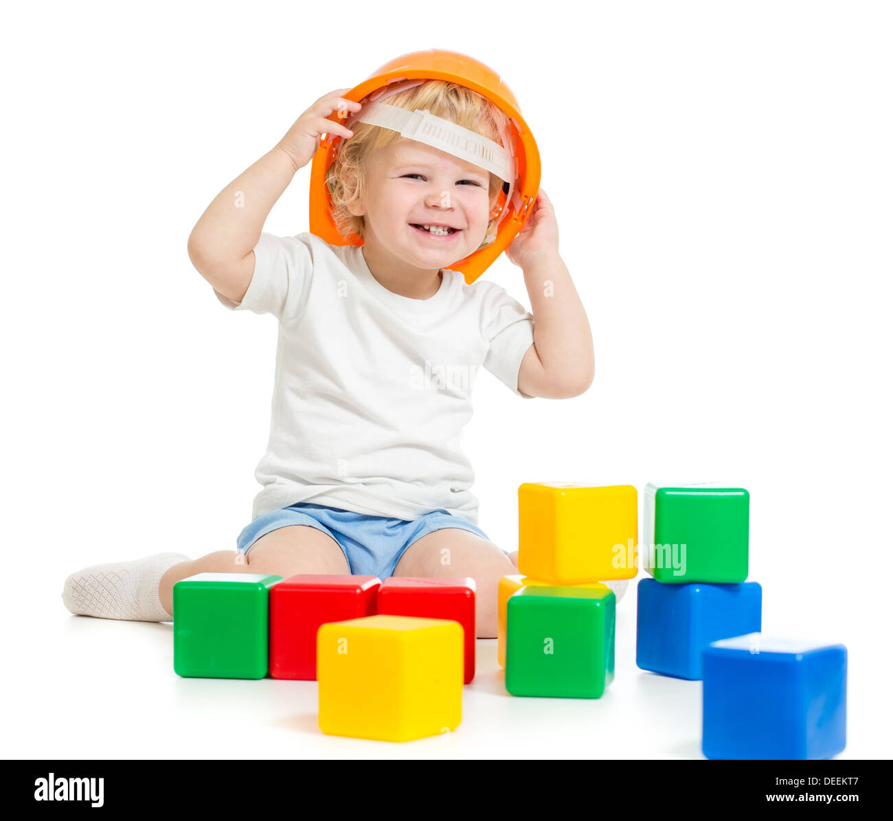 Niño feliz muchacho de sombrero duro jugando con coloridos bloques de construcción aislado en blanco Foto de stock