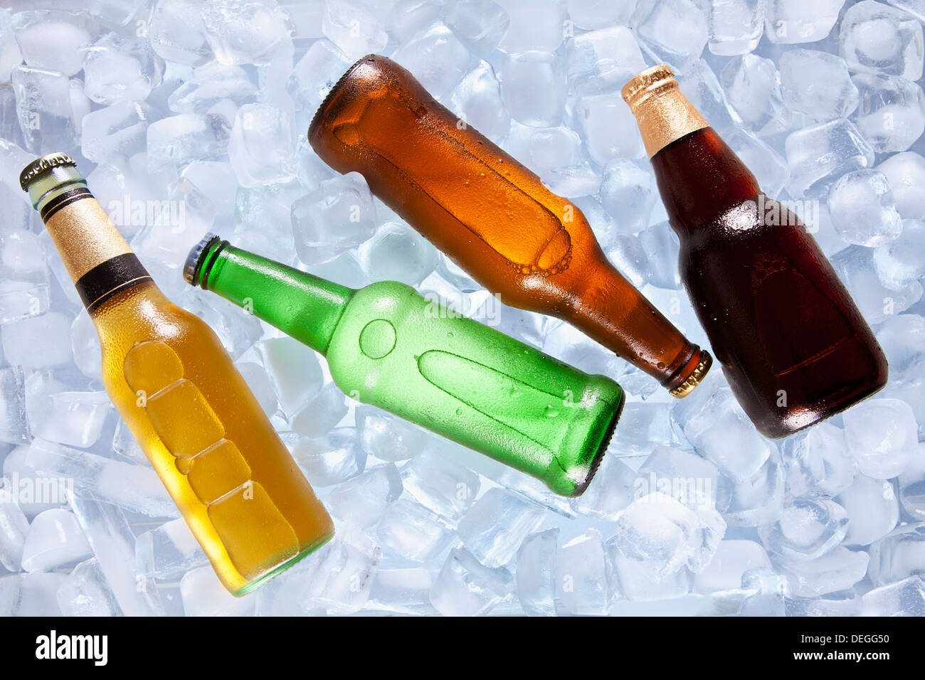 Cuatro tipos diferentes de botellas de cerveza en el hielo de enfriamiento. Foto de stock