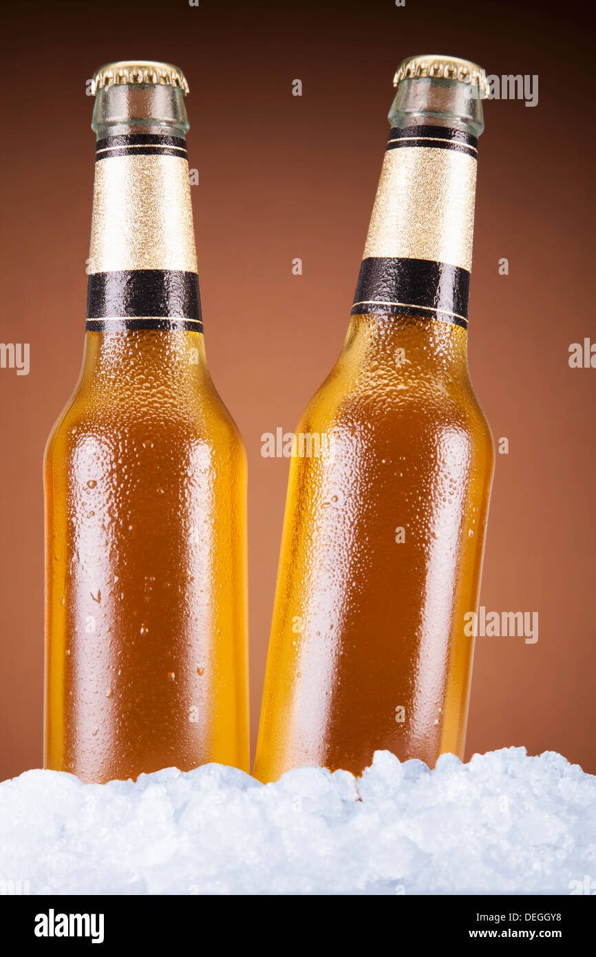 Dos botellas de cerveza sentado sobre el hielo sobre un fondo marrón. Foto de stock