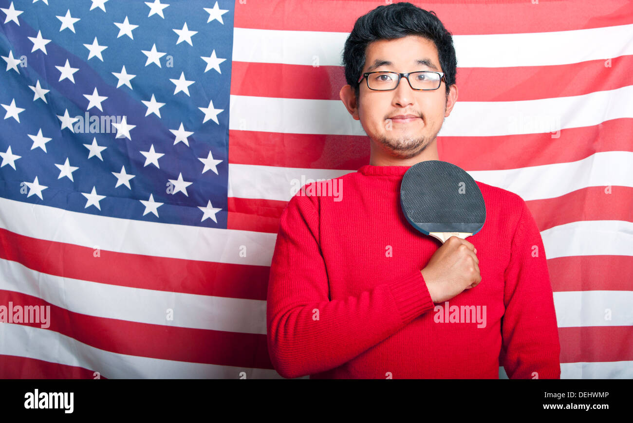 Orgulloso hombre asiático la celebración de pala de tenis de mesa contra la bandera estadounidense Foto de stock