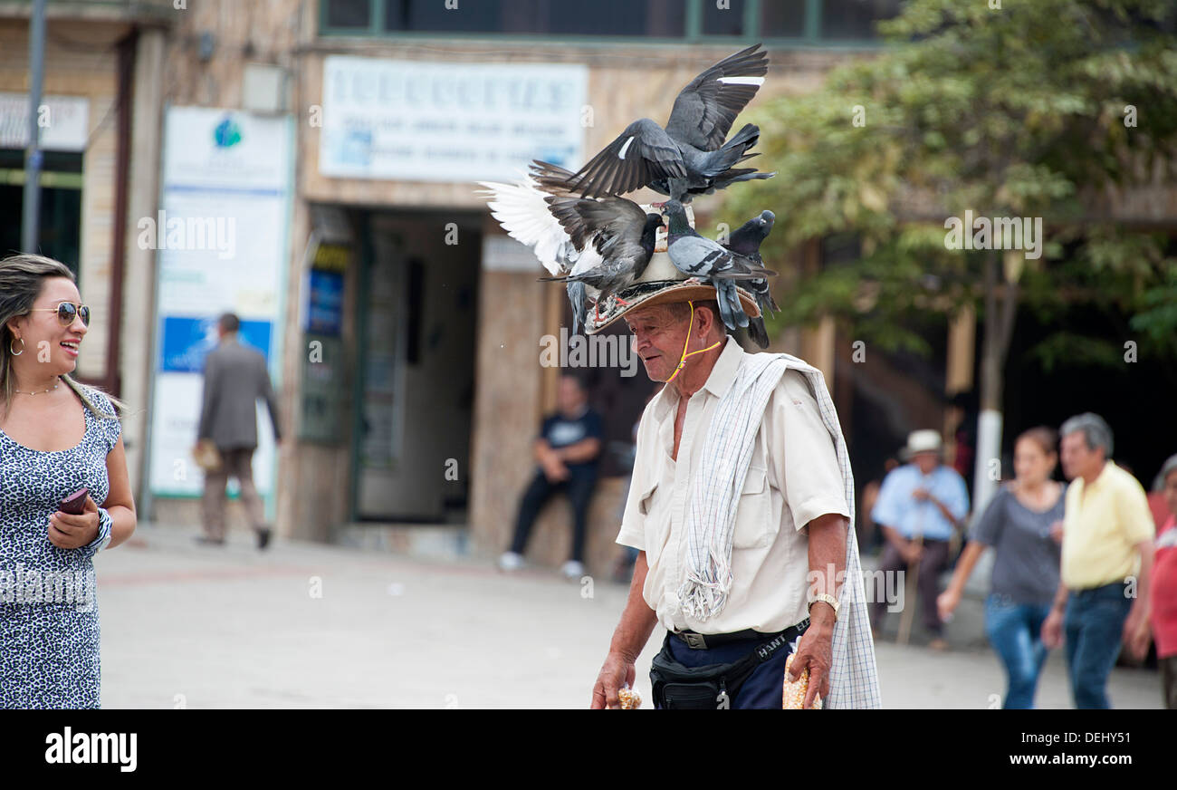 Turista se ríe con hombre colombiano con palomas en el sombrero en la plaza principal de Fusagasuga. Foto de stock