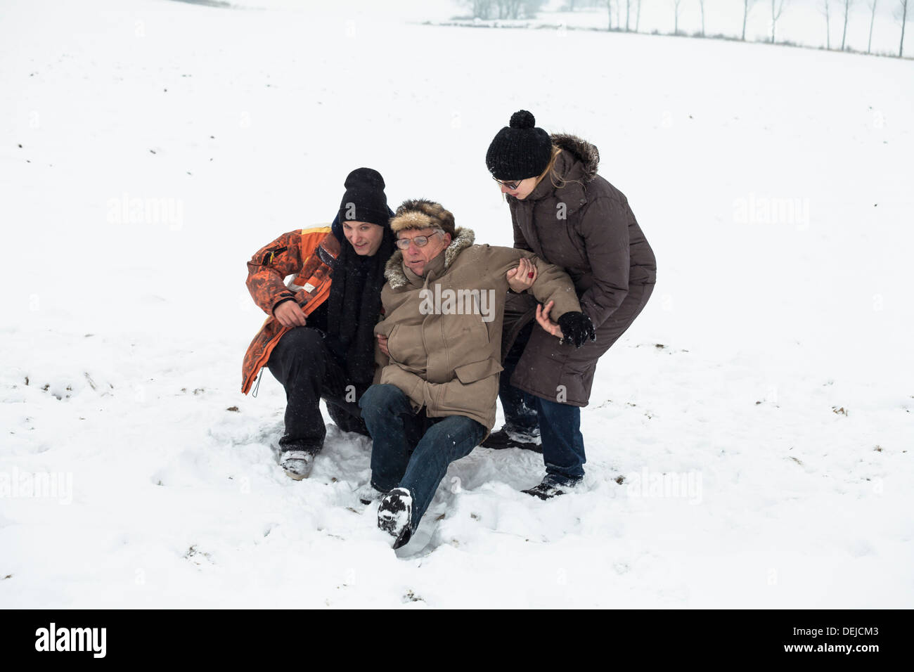 Par de jóvenes ayudando a altos hombre levantarse tras un accidente en la nieve. Foto de stock