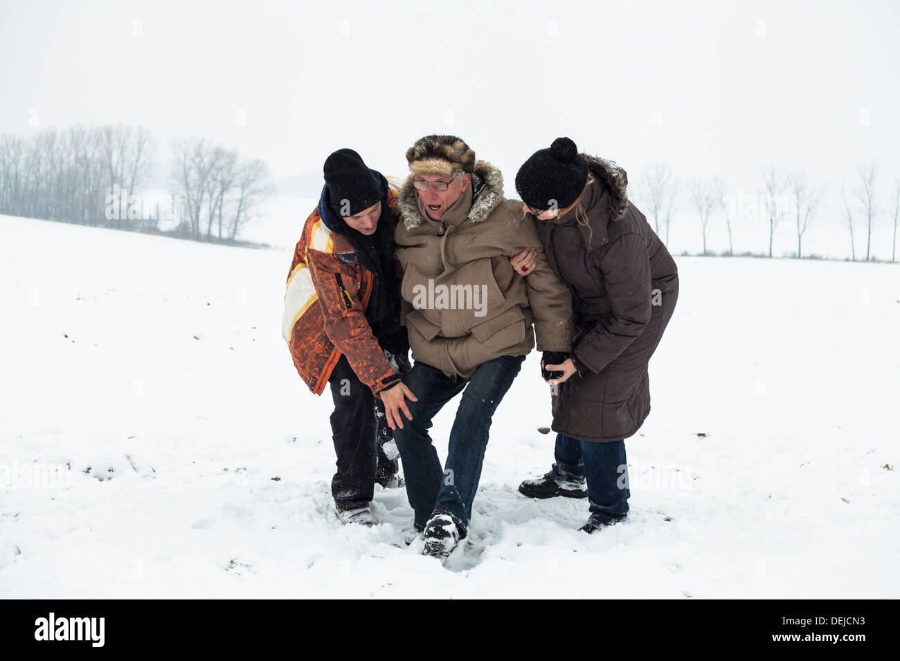 Par de jóvenes ayudando a altos hombre levantarse tras un accidente en la nieve en invierno. Foto de stock