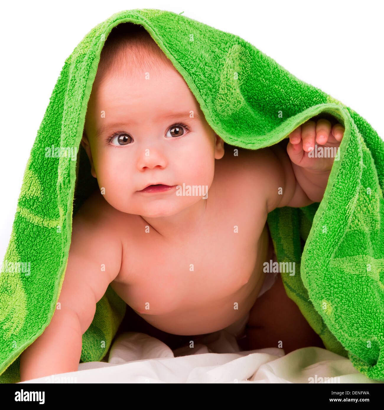 Curioso bebé mira desde debajo de una toalla verde Foto de stock