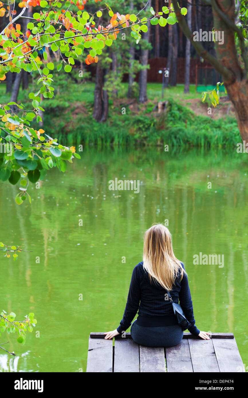 Chica solitaria por el lago en el parque sentado en un puente Foto de stock