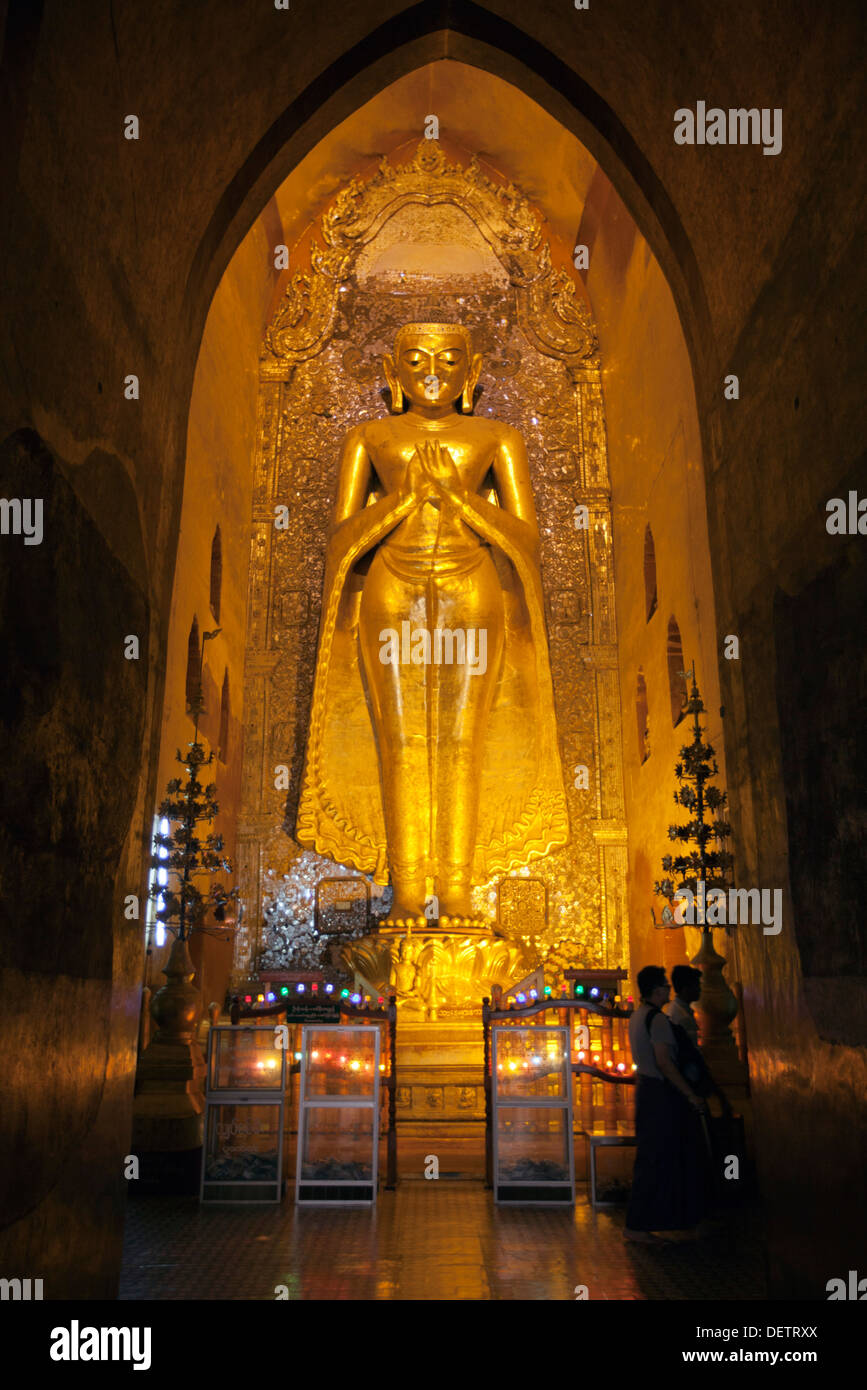 La gente camina más allá de una imagen de Buda en un templo en Bagan. Foto de stock
