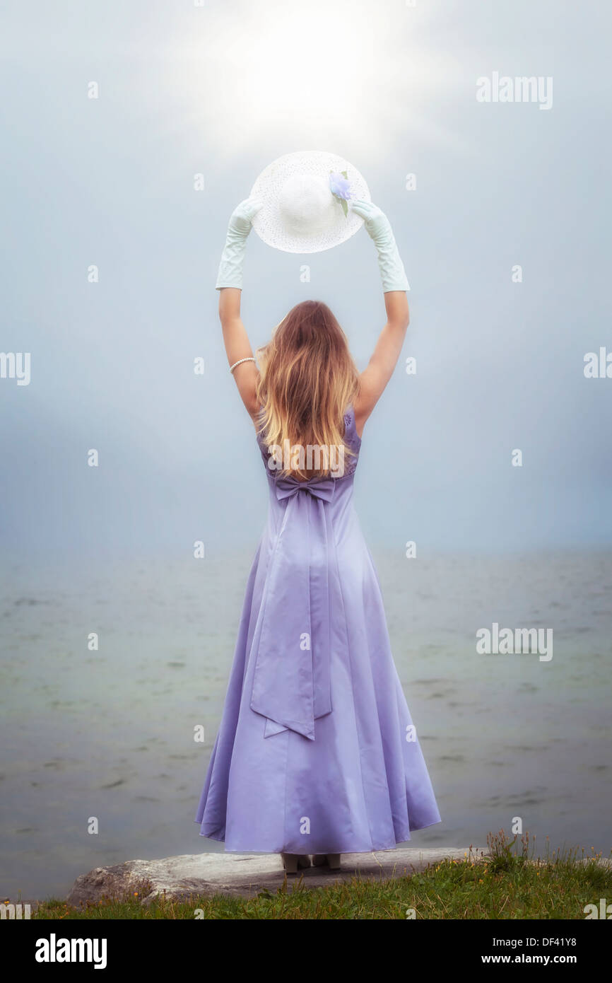 Una mujer en un vestido de púrpura está de pie en un lago con un sombrero para el sol Foto de stock
