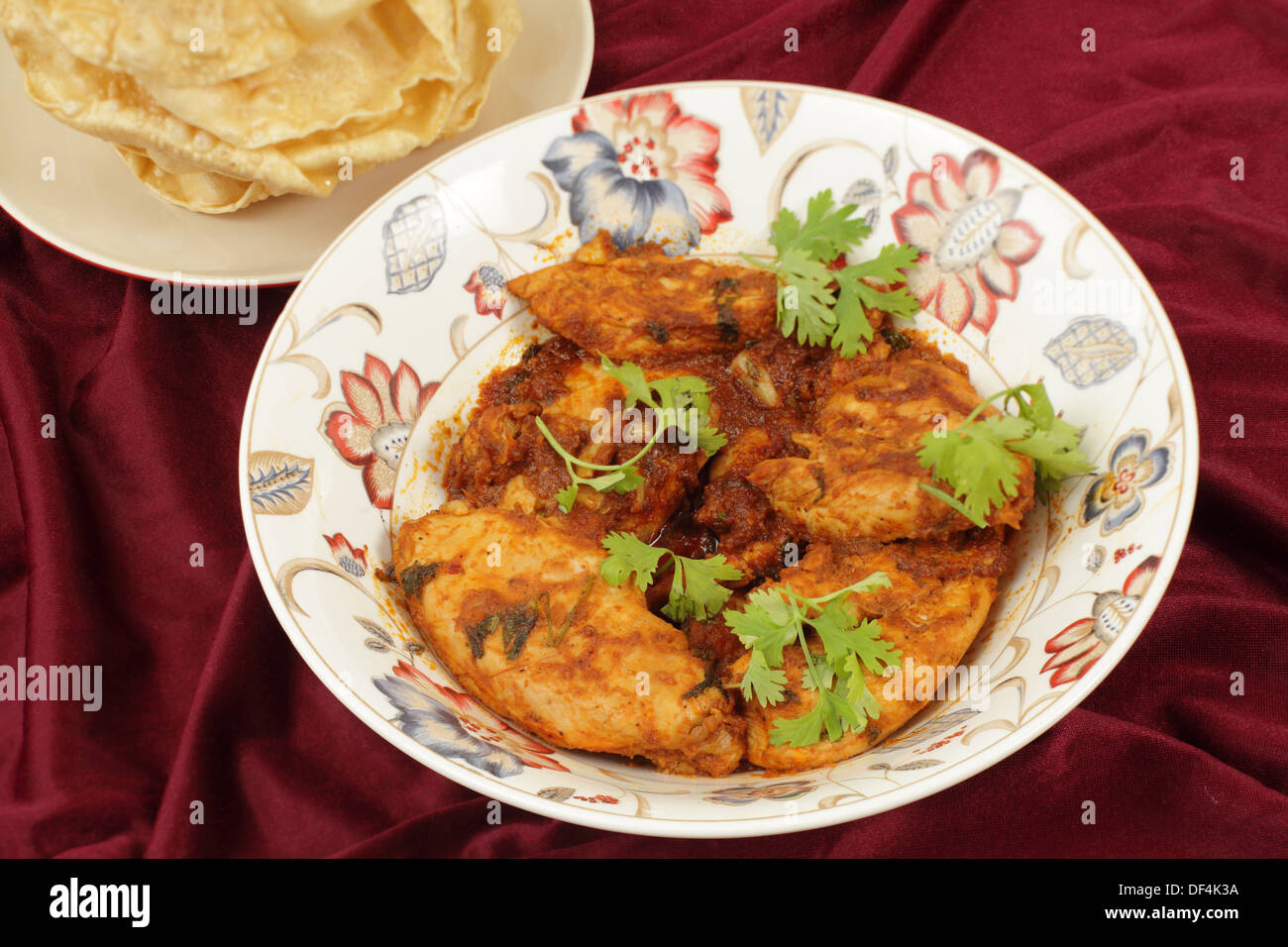Pollo de Cachemira en un recipiente para servir junto a un plato de pappadums Foto de stock