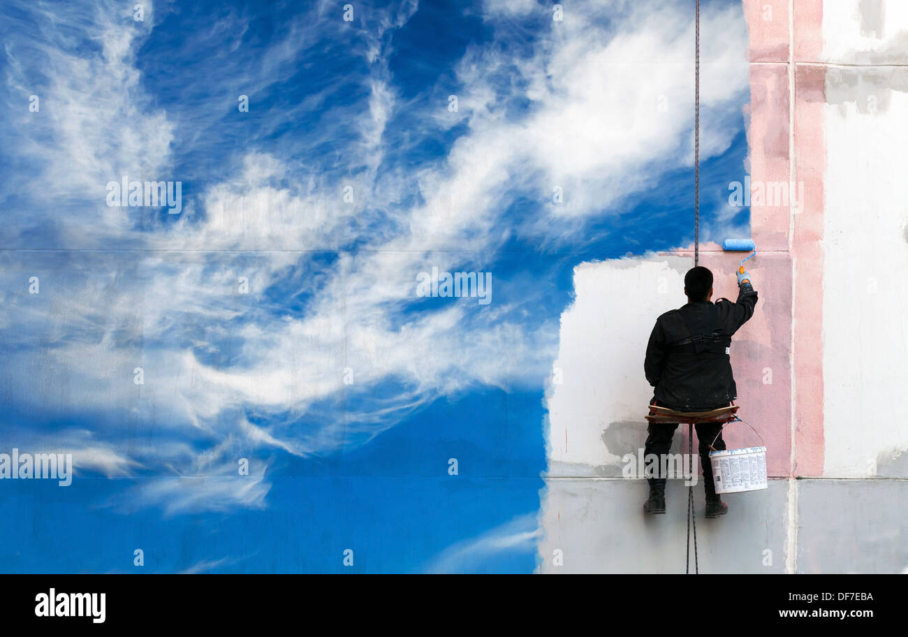 Pintor pinta brillante cielo azul sobre la muralla urbana Foto de stock
