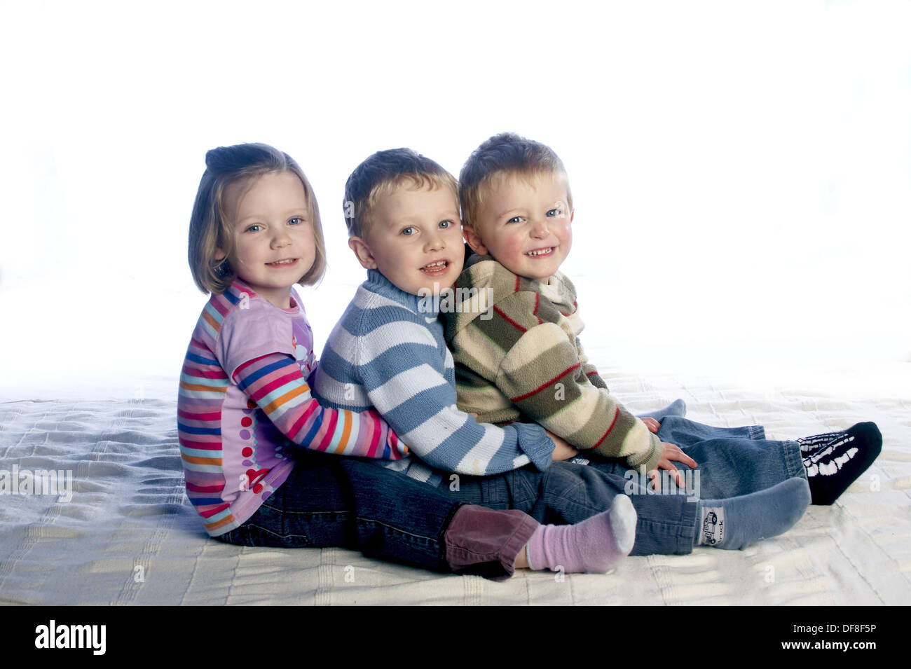 3,niños de tres años sentados en la fila en el suelo, sonriendo a la cámara  Fotografía de stock - Alamy