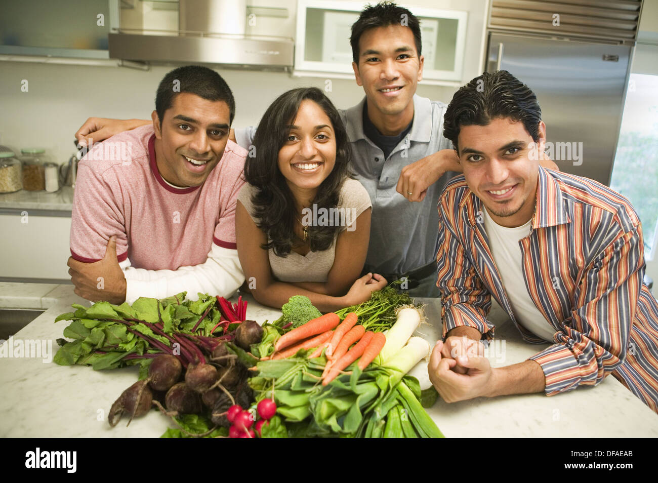 Grupo de jóvenes de etnias mixtas la celebración de verduras en la cocina Foto de stock