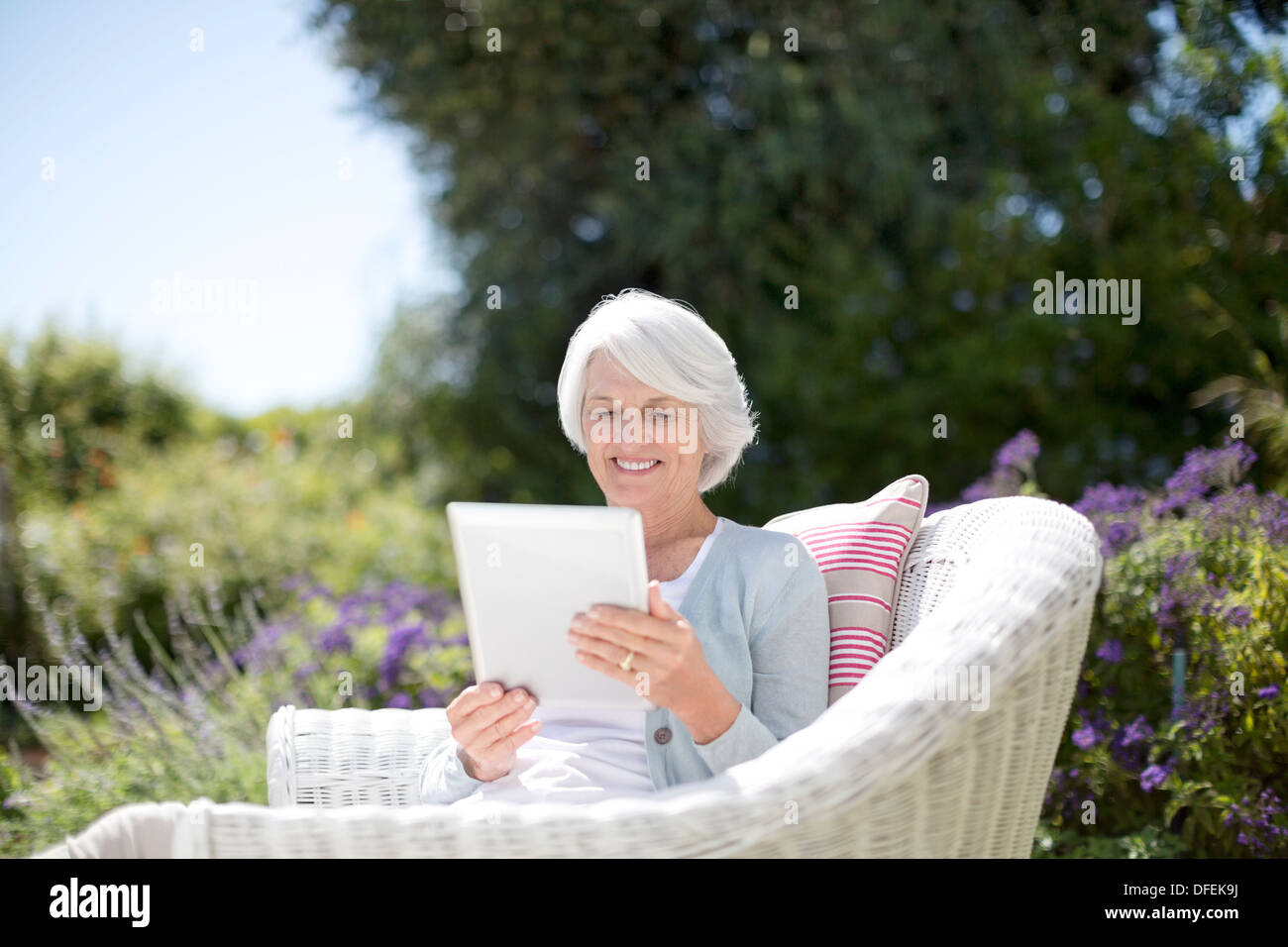 Mujer mayor utilizando digital comprimido en un sillón Foto de stock