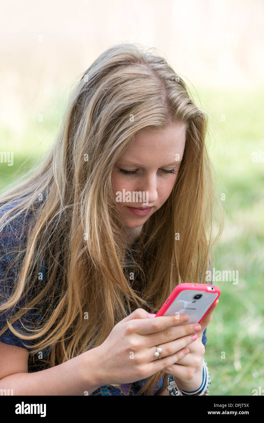 De joven, adolescente envejecido diecisiete,mensajes de texto en la celda /TELÉFONO MÓVIL AL AIRE LIBRE Foto de stock