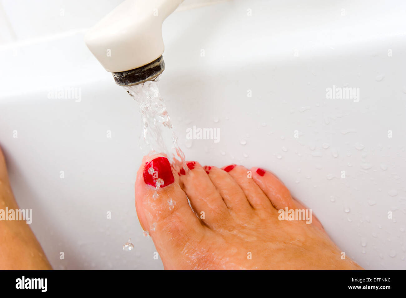 Una mujer mantiene su pie bajo el agua caliente del grifo del baño Foto de stock