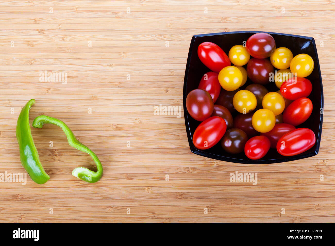 Tomates Cherry en la placa negra sobre la mesa de madera con rebanadas de pimiento verde Foto de stock