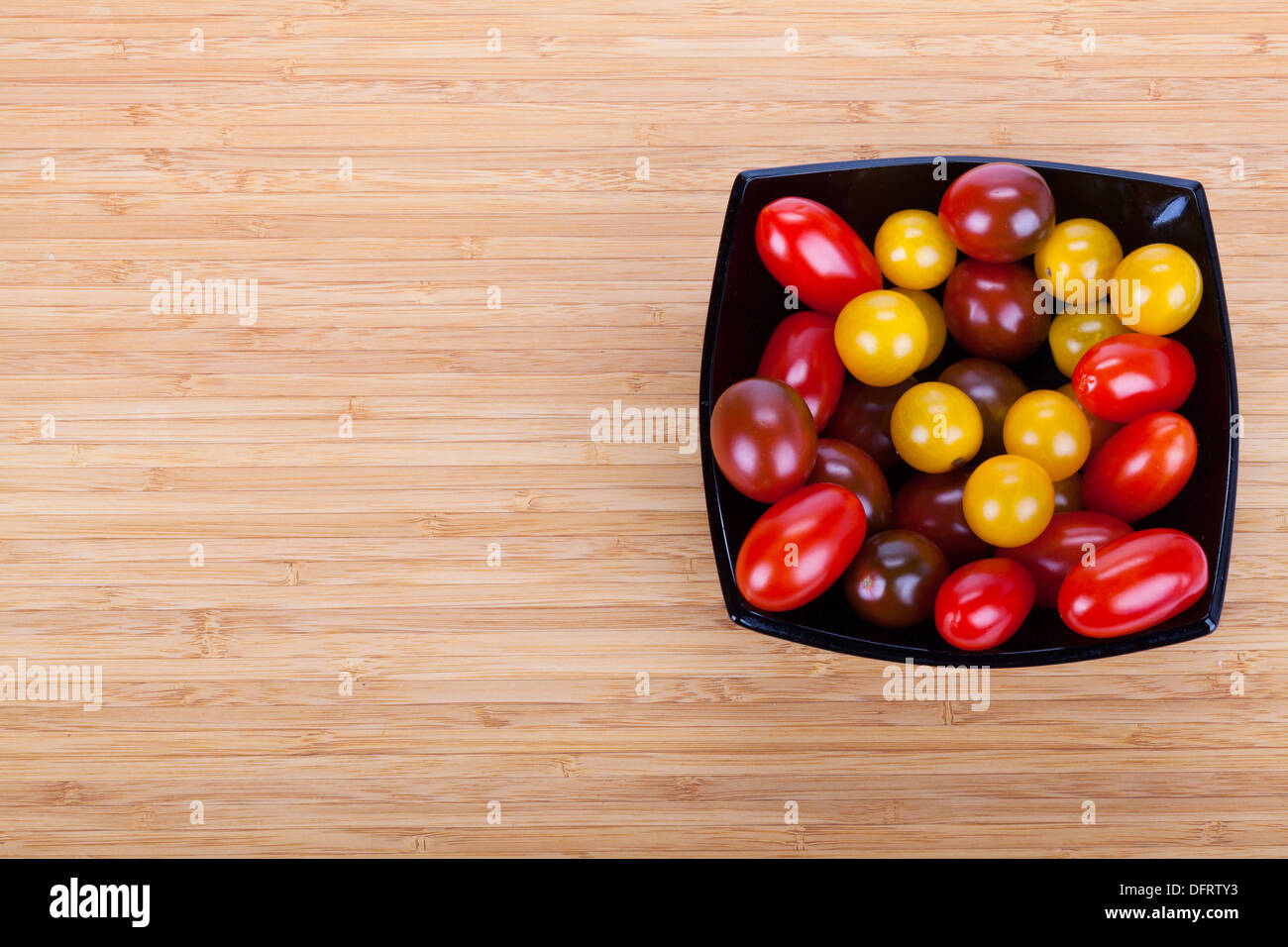 Сherry tomates en placa negra sobre la mesa de madera con rebanadas de pimiento verde Foto de stock