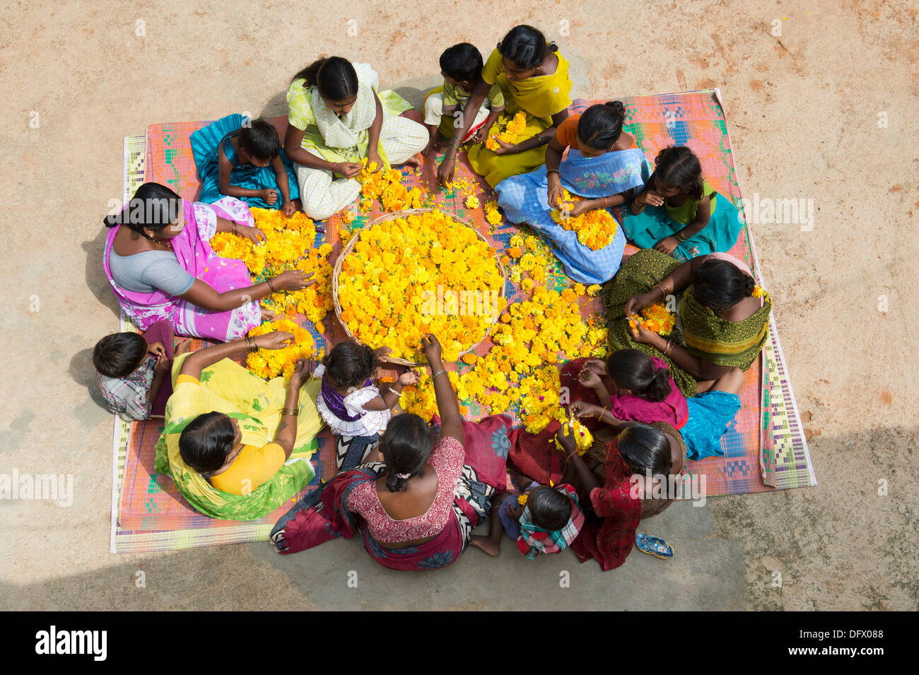 Aldea India mujeres y niños sentados alrededor de una cesta de flores de caléndula haciendo guirnaldas de flores. En Andhra Pradesh, India Foto de stock