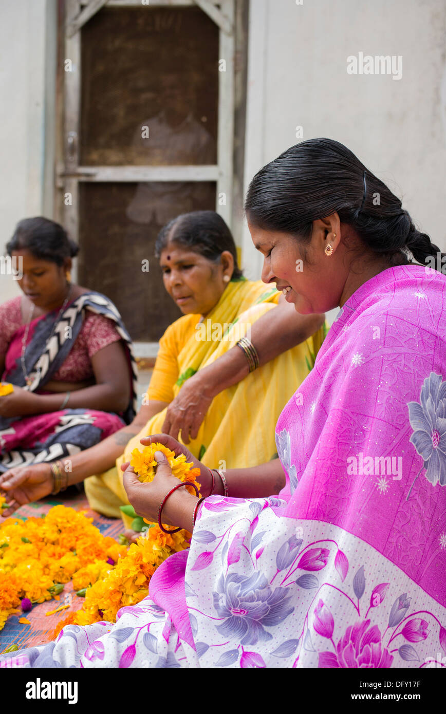 Aldea India mujeres sentadas alrededor de una cesta de flores de caléndula haciendo guirnaldas de flores. En Andhra Pradesh, India Foto de stock